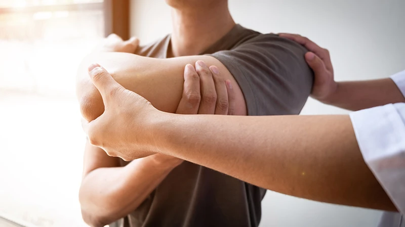 Physiotherapeut führt gemeinsam mit Patient eine Dehnübung für die Rotatorenmanschette durch Physiotherapeut führt gemeinsam mit Patient eine Dehnübung für die Rotatorenmanschette durch