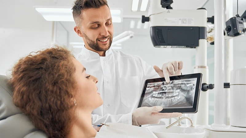 Implantologie Wagenfeld | Arzt zeigt Patientin das Gebiss auf einem Tablet Implantologie Wagenfeld | Arzt zeigt Patientin das Gebiss auf einem Tablet
